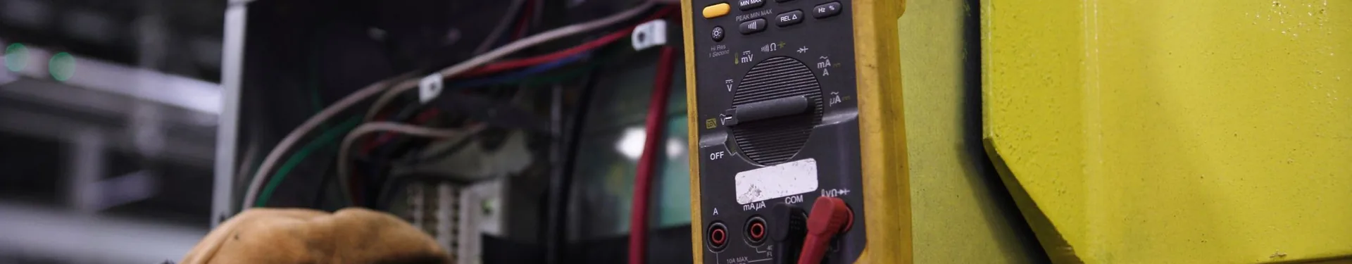 Gloved hands testing an electrical cabinet with a multimeter